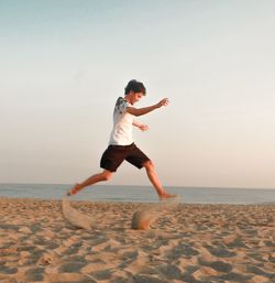 Full length of man jumping on beach against clear sky