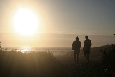 Rear view of silhouette people walking on beach at sunset