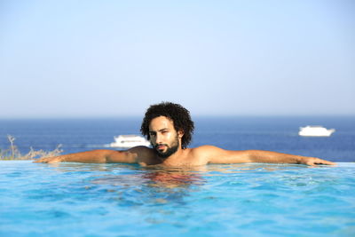 Portrait of young man resting in infinity pool against clear sky
