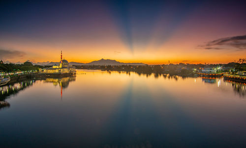 Scenic view of lake by buildings against sky during sunset