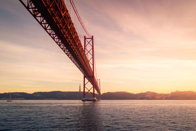 From below rusty metal mooring poles located on shore of tagus river under 25 de abril bridge at sundown in lisbon, portugal