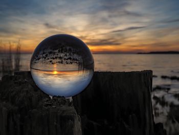 Close-up of crystal ball on wooden post at beach during sunset