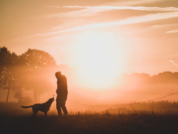 Silhouette teenager boy with dog against sky during sunset