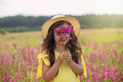 A beautiful playful little girl in a straw hat, holds a bouquet of burgundy viscaria flowers