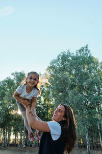 Young woman smiling while standing against trees against sky