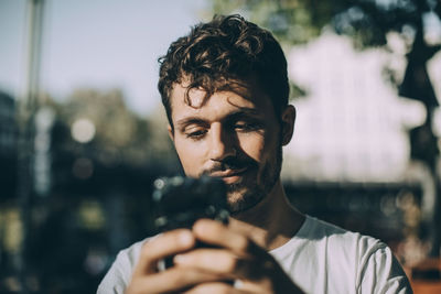 Portrait of young man holding camera outdoors