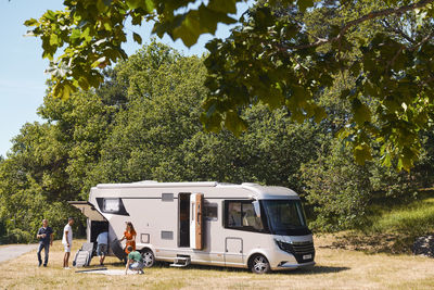 Family unloading motor home parked against trees at trailer park