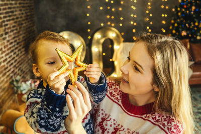 Mother and son with gift sitting on chair against christmas tree