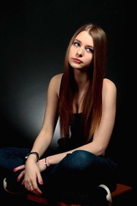 Thoughtful young woman sitting against black background