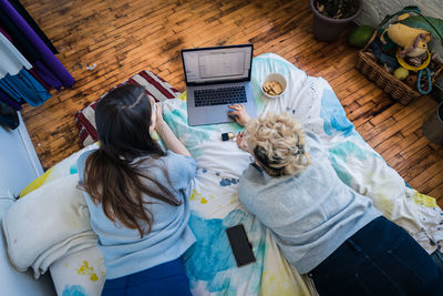 High angle view of female friends using laptop while resting on bed in bedroom at home