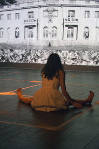 Rear view of woman sitting against building in city