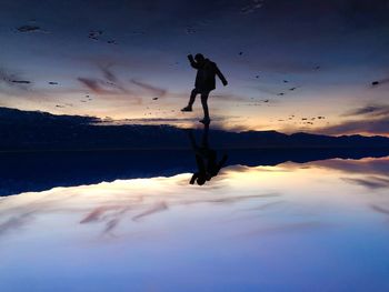 Silhouette man standing in sea against sky during sunset