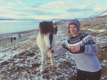 Portrait of woman feeding horse while standing on field against sky