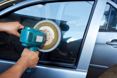 Cropped hands of man polishing car window in auto repair shop