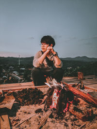 Young man sitting on mountain against clear sky