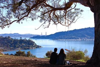 Rear view of people sitting by lake against sky