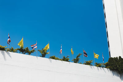 Low angle view of flags against buildings against clear blue sky