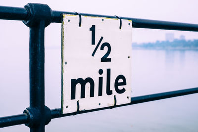 Close-up of sign on railing against sky