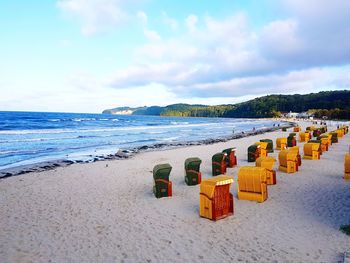 Hooded chairs on beach against sky