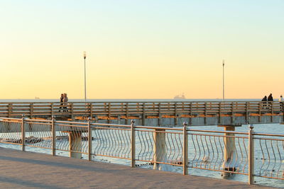 People on pier at beach against clear sky during sunset