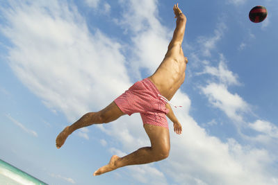 Shirtless man playing volleyball at beach against sky