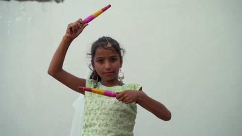 Portrait of young woman with arms raised standing against wall