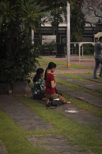 People sitting on sidewalk against plants