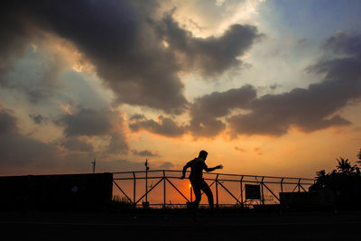 Silhouette man standing on bridge against sky during sunset