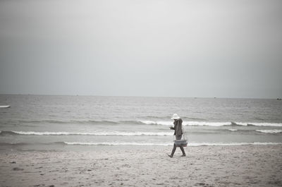 Side view of fisherman walking on beach against clear sky