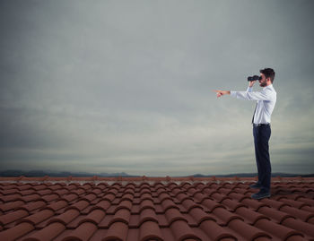 Side view of young man standing on land against sky