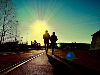 Silhouette men on sidewalk against sky during sunset
