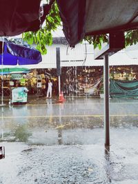 Wet street by swimming pool against buildings in city during rainy season