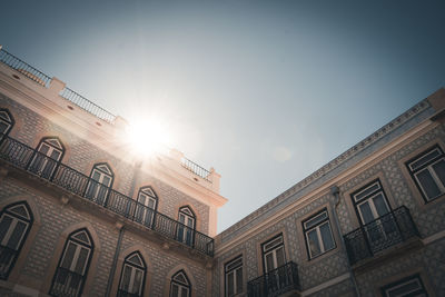 Low angle view of sun streaming through building against sky
