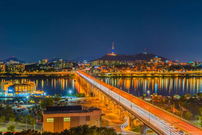 Illuminated bridge and buildings against sky at night