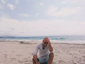 Man sitting on beach against sky