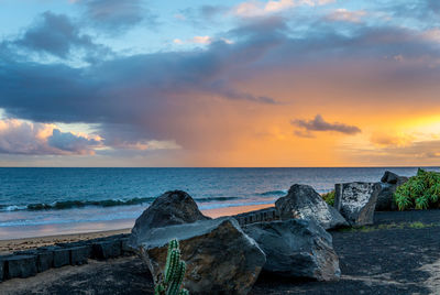 Rocks by sea against sky during sunset