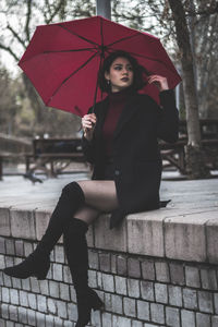 Woman holding umbrella sitting against trees