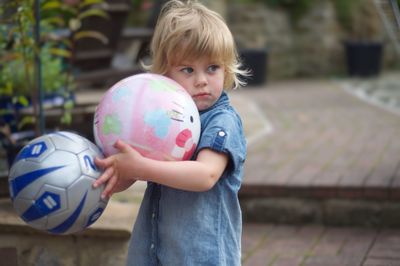 Cute boy holding ball while standing outdoors