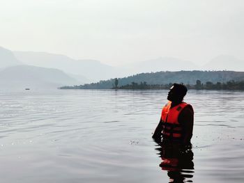 Rear view of man standing in lake against sky