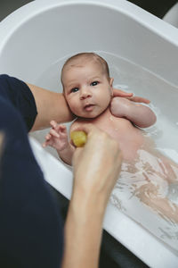 Cropped hands of mother bathing son in bathtub at home