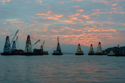 Cranes at commercial dock against sky during sunset