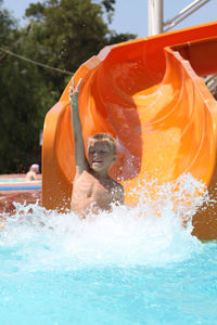 Shirtless boy sitting on slide in water