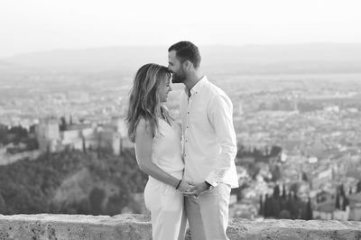 Side view of young romantic couple standing by retaining wall