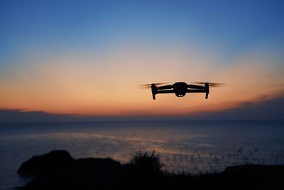 Silhouette bird flying over sea against sky during sunset