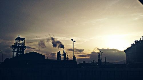 Silhouette of factory against sky