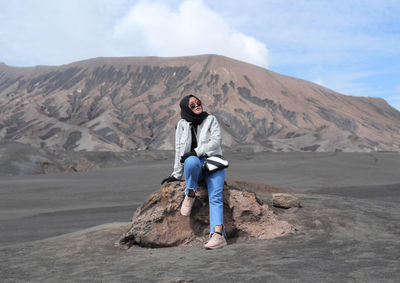 Full length of woman sitting on rock against mountain