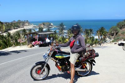 Man sitting on motorcycle at street against sea during sunny day