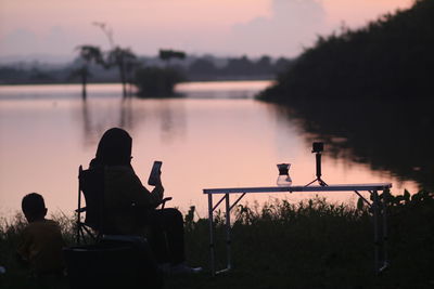 Rear view of man sitting on pier against lake during sunset