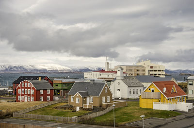 Colorful houses, a church and the hospital under a cloudy sky, with the fjord in the background
