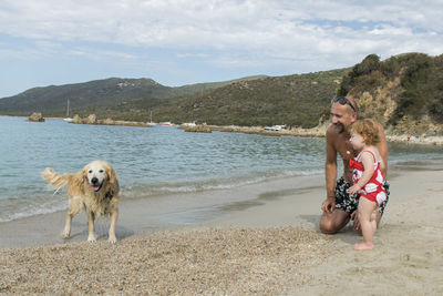 Happy father with daughter looking at dog at beach